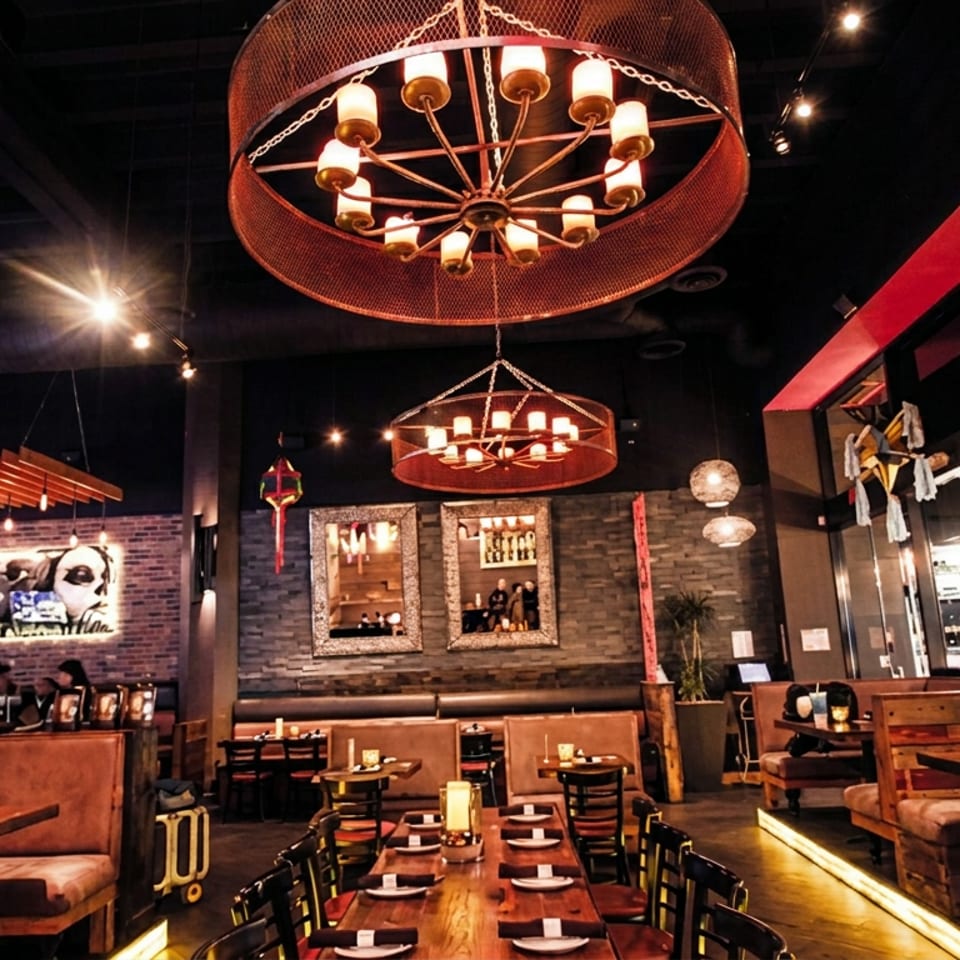 Warmly lit restaurant interior with leather booths, wooden tables, exposed brick walls, and large circular chandeliers.