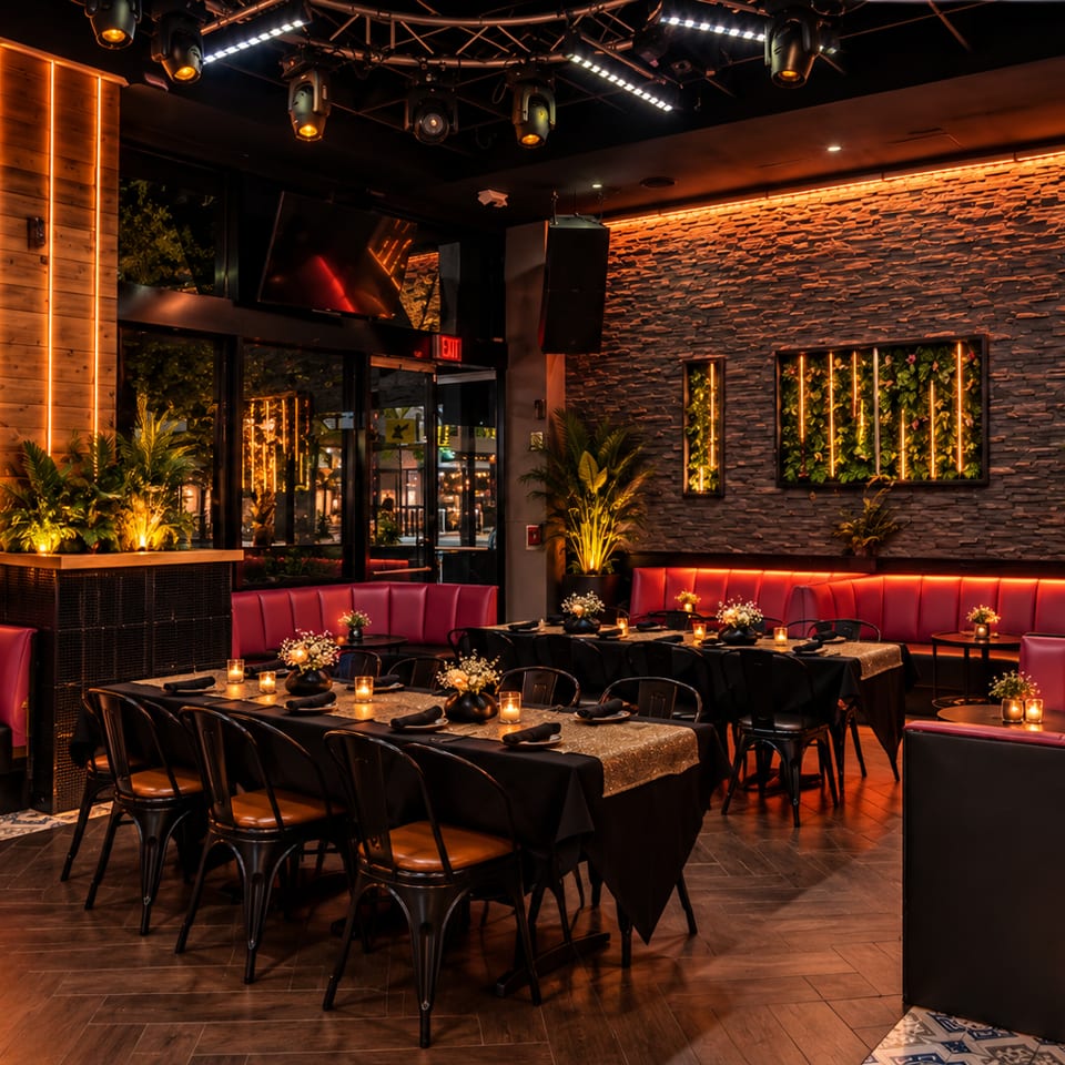 Upscale restaurant interior with red banquettes, candlelit tables, lush plants, stone walls, and warm dramatic lighting.