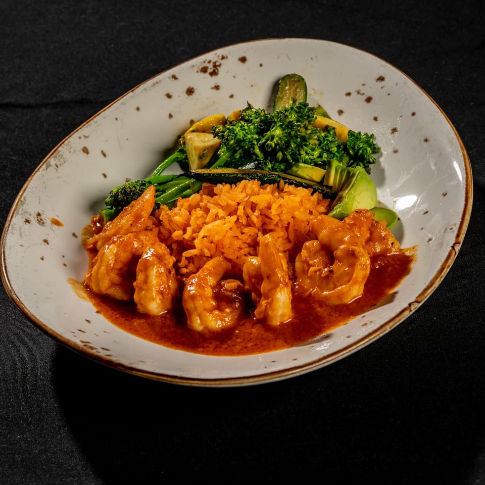 Plate of glazed shrimp with orange rice and assorted roasted vegetables on a rustic ceramic dish.